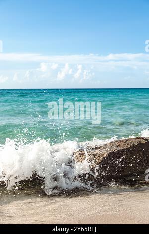 Enjoy the view of the Caribbean Sea from Varadero province in Cuba, where waves crash against a rocky foreground on a sunlit, sandy beach. Stock Photo