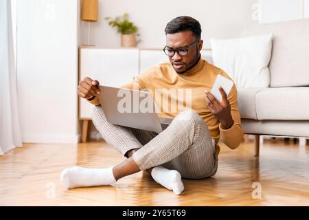 Black Man Holding Phone Working On Laptop On Floor Indoor Stock Photo
