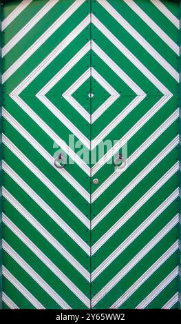 Close-up view of a vibrant green door featuring white stripe patterns and metallic details, showcasing symmetrical design and texture Stock Photo