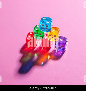 A stack of multicolored transparent dice casts vivid shadows on a pink surface, illustrating a play of light and color Stock Photo