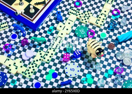 An eclectic array of game pieces, including chess figures, dice, and dominoes, scattered across a checkered surface, highlighted with vibrant, saturat Stock Photo