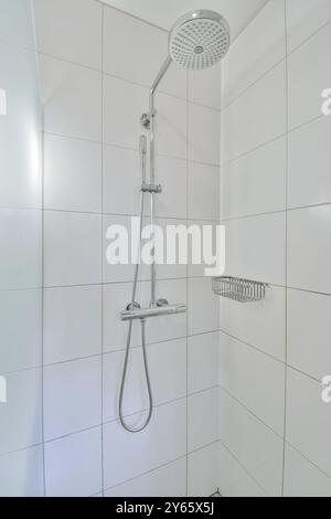 A sleek, modern shower head and fixture mounted on glossy white tiles in a bright, clean bathroom. Stock Photo