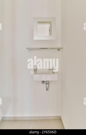 A sleek and modern hand wash basin with a stainless steel faucet and a small square mirror mounted on a clean, white wall in a minimalist bathroom des Stock Photo