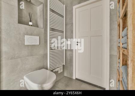 A contemporary bathroom featuring a towel heater, a wall-mounted toilet, and a wooden towel shelf, all in a neutral color palette. Stock Photo