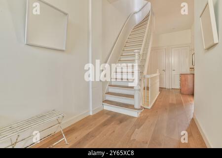 A well-lit hallway featuring a white elegantly curved staircase, hardwood floors, and minimalist decor. Stock Photo