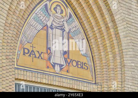 Vibrant mosaic of an angel with outstretched wings and the Latin phrase "Pax Vobis" on a church exterior, symbolizing peace. Stock Photo