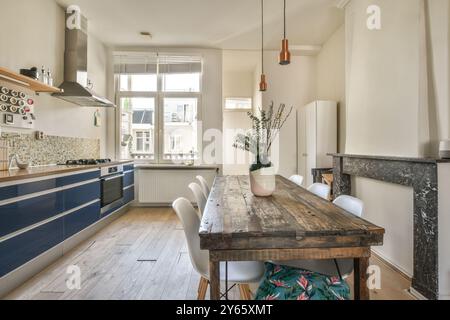 Modern kitchen with blue cabinetry and a rustic dining table set against a backdrop of neutral walls and hardwood floors. Stock Photo