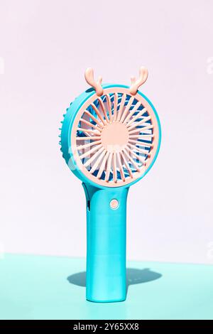 This image showcases a modern portable hand fan in a vibrant blue color, featuring a unique antler design on top, set against a soft pink background Stock Photo