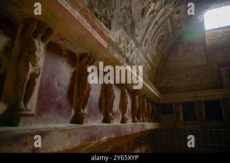 This stock image captures a series of ancient Roman sculptures lined along the wall inside a historical Pompeii house, adorned with beautifully preser Stock Photo
