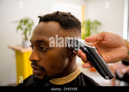A close-up view of a skilled barber giving a precise haircut to a black man in a coast-themed barber shop The image shows the use of modern tools and Stock Photo