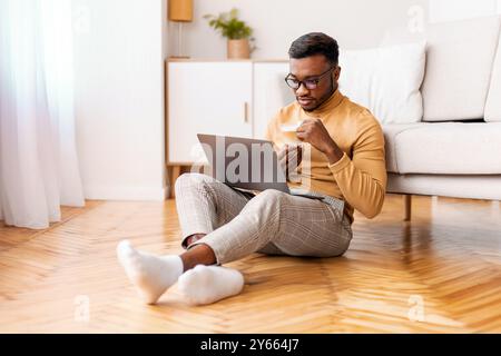 Afro Man Working On Laptop Having Coffee Sitting On Floor Stock Photo