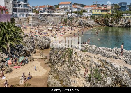 People climbing on the huge rocks at Praia da Rainha and the Estoril Sol Residence building in the Portuguese city of Cascais, Cascais, Portugal. Stock Photo