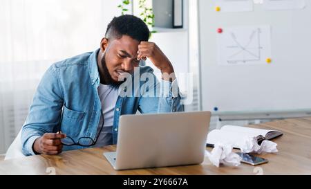 Stressed african worker looking to laptop screen with despair Stock Photo