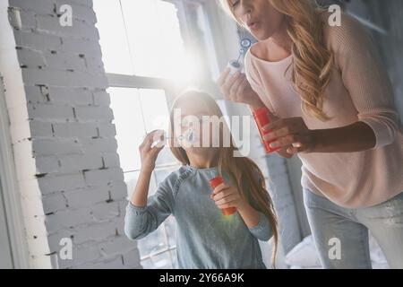 Fun time. Mother and daughter blowing soap bubbles while spending time at home Stock Photo