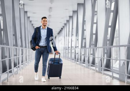 Portrait of young middle eastern man walking in airport terminal with luggage Stock Photo