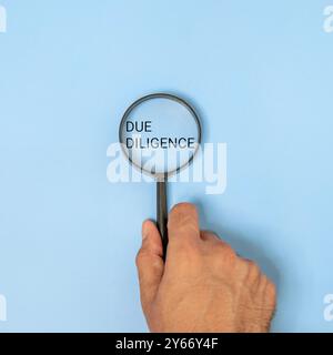 A hand holding a magnifying glass over the words “DUE DILIGENCE” on blue background. Business, finance, law, research concept. Stock Photo