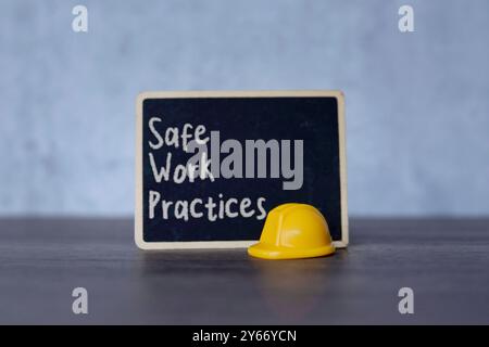 Small chalkboard with the text “Safe Work Practices” and yellow hard hat. Concepts of safety, precaution, and standards in the workplace. Stock Photo