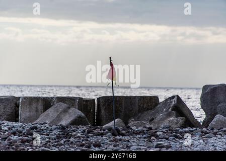 flag silhouetted at sunset over the pebble beach and the piers of the Atlantic Ocean at Ponta Do Sol in Madeira Portugal Stock Photo