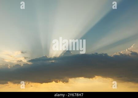 The sun shines behind the clouds. Rays shining from behind the clouds at sunset. Stock Photo