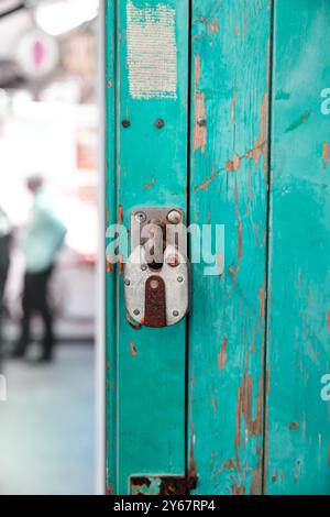 a close-up view of a worn, rusted padlock on a turquiose or teal blue green painted door showing signs of wear and tear. The lock is old and worn, wit Stock Photo