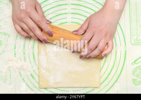 Hands rolling dough with a wooden rolling pin on a green baking mat. Culinary preparation. Close-up food photography. Concept of baking. Stock Photo