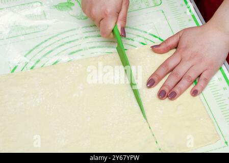 Hands cutting dough with a green knife on a measurement mat. Close-up shot. Concept: baking preparation, kitchen activities, culinary skills. Stock Photo