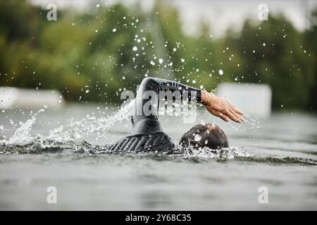 Side view of strong man swimming in forest lake with water splashes and wearing wet suit practicing for triathlon Stock Photo