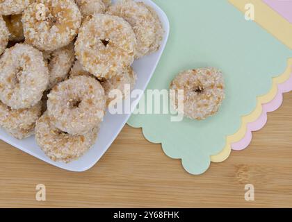 Cropped angle view of a square plate with round crumb donuts on a light wood table, one donut isolated on green paper napkin with pink and yellow napk Stock Photo
