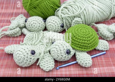 Parts of turtle and whole completed turtle on red patterned mat with skein and ball of yarn and crochet hook. Hand made childrens toys. Stock Photo