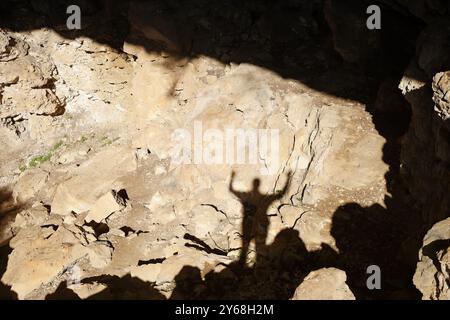 A shadow of a person with raised arms cast on a sunlit rocky cave floor, with rough terrain and bright sunlight creating contrast. Stock Photo