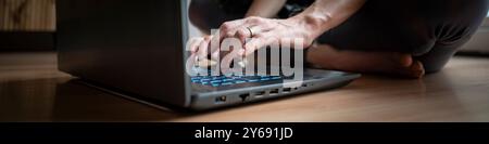 Wide closeup view image of female hands using laptop computer on domestic living room floor. Low angle view. Stock Photo