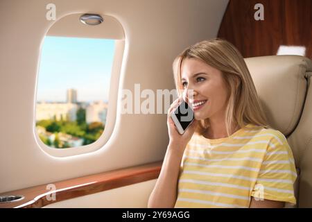 Woman talking on phone in cabin while airplane taking off or landing, view on city from window Stock Photo