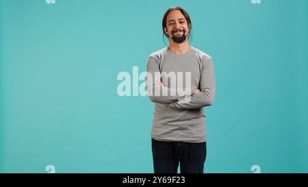 Portrait of cheerful Arab man smiling, looking pleased, isolated over blue studio background. Happy expressive person stylishly dressed grinning, feeling satisfied, camera A Stock Photo