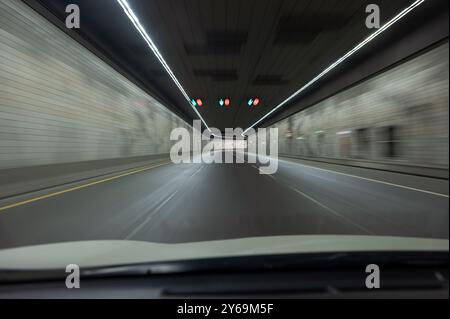 Inside a modern vehicular tunnel, smoothly paved roads with marked lanes, horizontal panel walls, continuous overhead lights Stock Photo