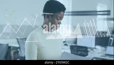 Analyzing documents, businesswoman with data charts and graphs image over office background Stock Photo