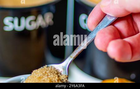 Freshly poured espresso,hot and ready to drink at breakfast,a silver spoon about to mix in brown sugar to sweeten,on a wood board, a bread roll,sugar Stock Photo