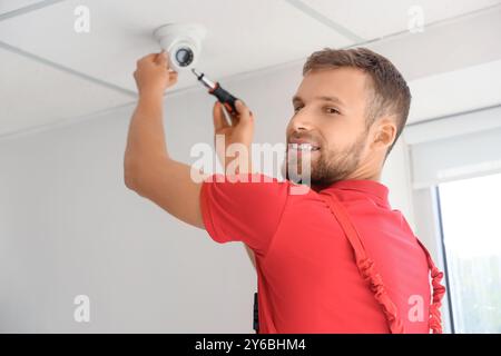 Male worker installing alarm system on ceiling in room Stock Photo