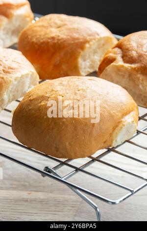 Freshly baked bread rolls cobs cooling down on a cooling rack on a wooden board. Home baking concept Stock Photo