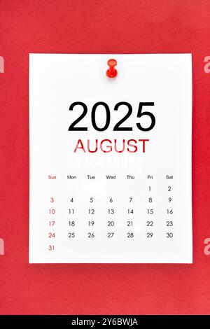 August 2025 calendar page with push pin on red color background. Stock Photo