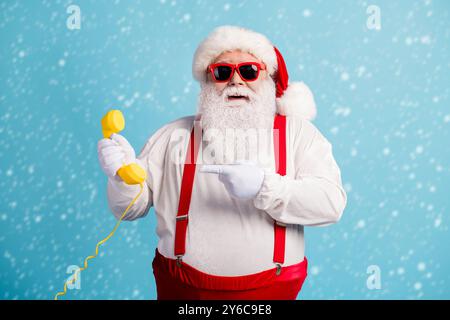 Portrait of his he nice attractive cheerful funky white-haired Santa holding in hand demonstrating yellow retro telephone isolated over bright vivid Stock Photo