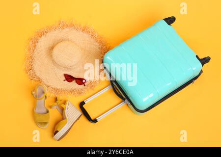 Turquoise suitcase, straw hat, shoes and sunglasses on yellow background, above view Stock Photo