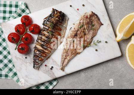 Board with delicious grilled mackerel, tomatoes, spices and lemon on grey table, flat lay Stock Photo