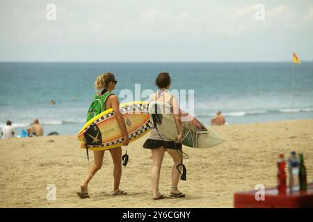 Women tourists carry surfboards, as they are walking on Kuta beach, Badung, Bali, Indonesia. Stock Photo