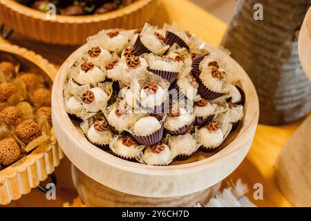 A close-up view of assorted gourmet chocolates and truffles displayed in a wooden bowl at a dessert table. Stock Photo