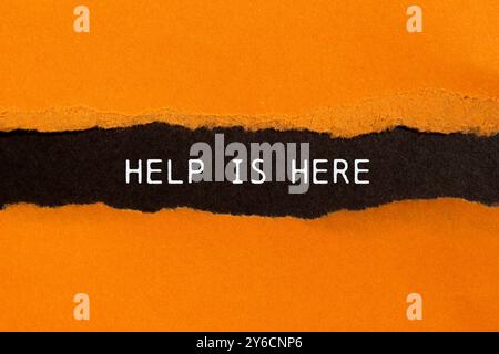 Help is here message written on ripped torn orange paper on black background. Conceptual help is here symbol. Copy space. Stock Photo