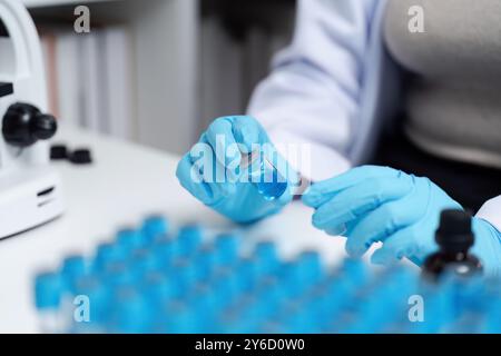 Scientist in Laboratory Handling Blue Liquid Samples with Microscope and Test Tubes Stock Photo