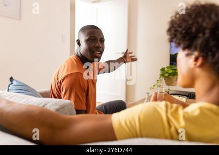 At home, Two diverse male friends sitting on couch, talking and watching television together Stock Photo