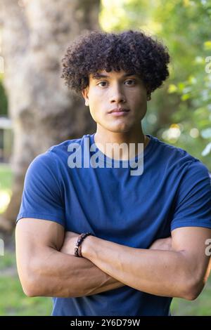 Man with curly hair standing outdoors with arms crossed, looking confident Stock Photo