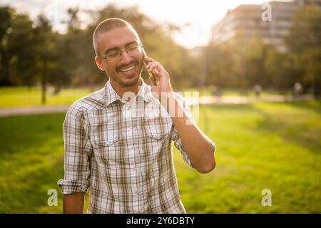Portrait of cheerful adult man in park who is talking on phone. Stock Photo