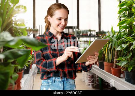 A woman efficiently manages her local plant nursery shop using a digital tablet, leveraging technology to streamline inventory tracking and enhance cu Stock Photo